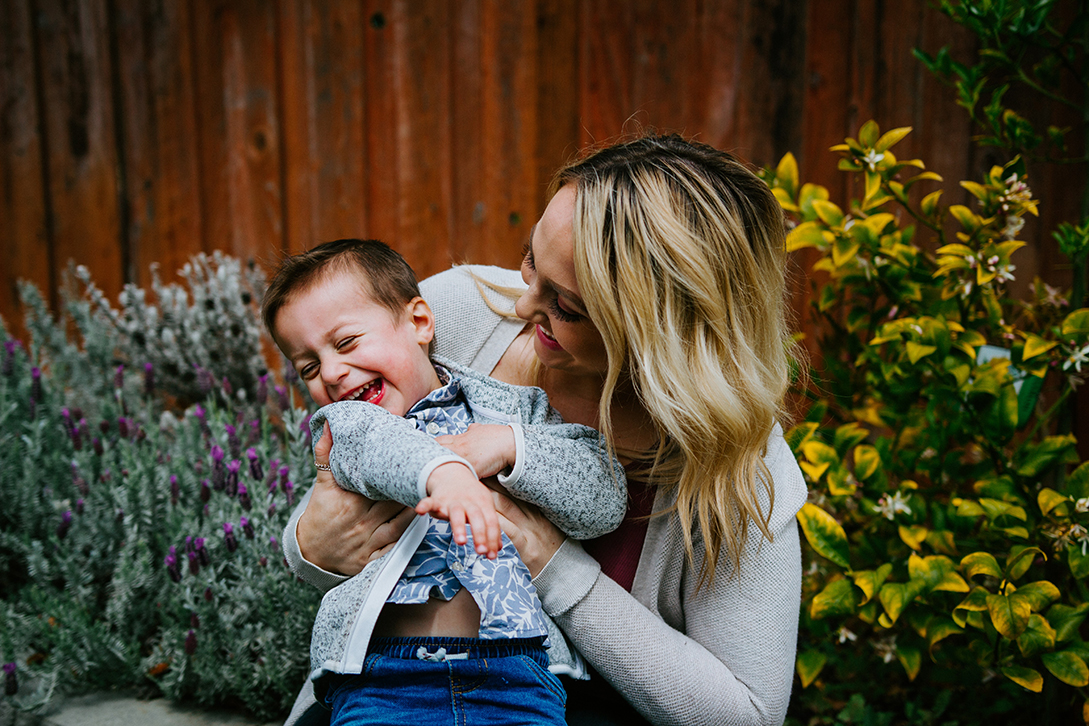 Photo of mom with young son laughing in front of flowers