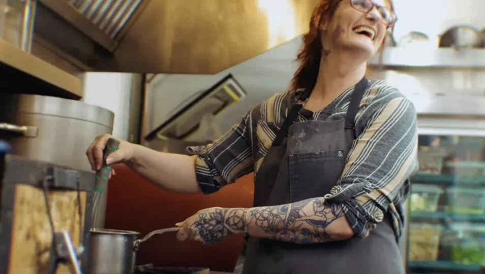 Fotografía de una mujer riendo mientras revuelve algo en la estufa.