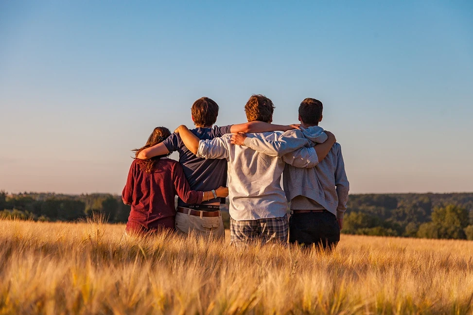 Foto de cuatro personas abrazadas en un campo.