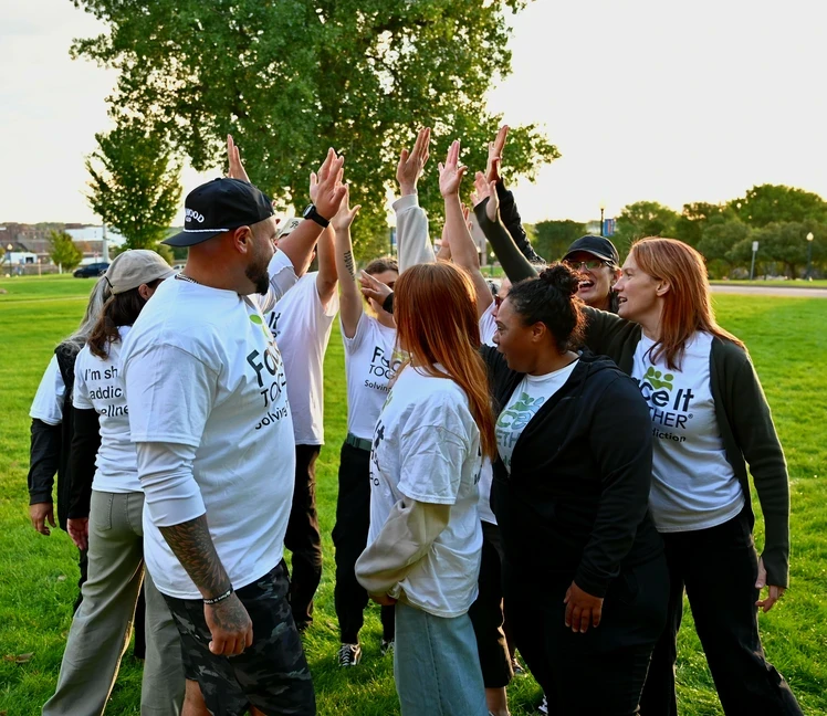 Photo of people in a circle with their hands up