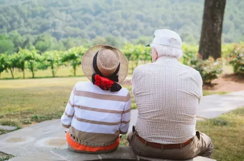 Photo of older couple sitting on a bench facing scenery