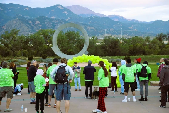 Photo of speaker in front of green balloon arch and mountains during morning walk