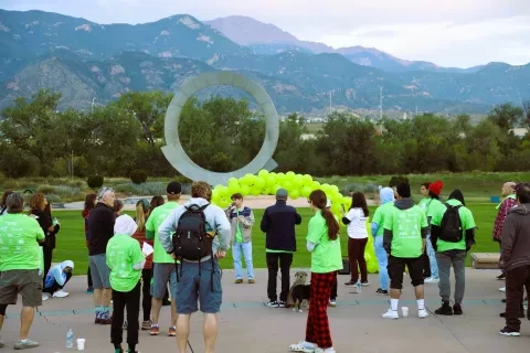 Fotografía de un orador frente a un arco de globos verdes y montañas durante una caminata matutina