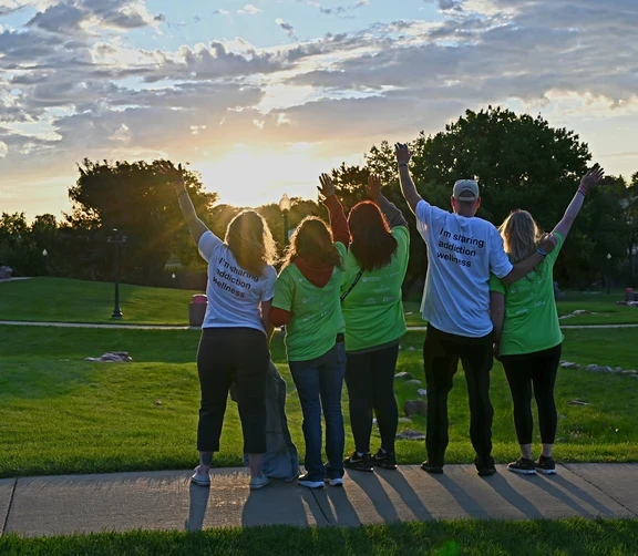 Photo of backs of people celebrating in front of sunrise